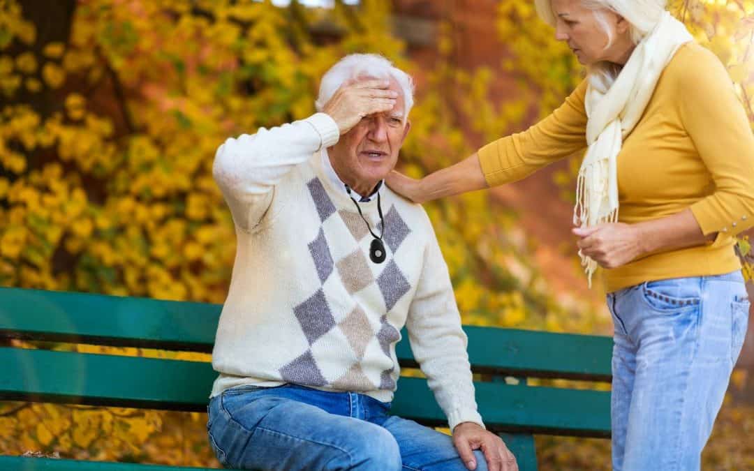 Elderly man experiencing a medical emergency with a caregiver nearby using a personal alarm.